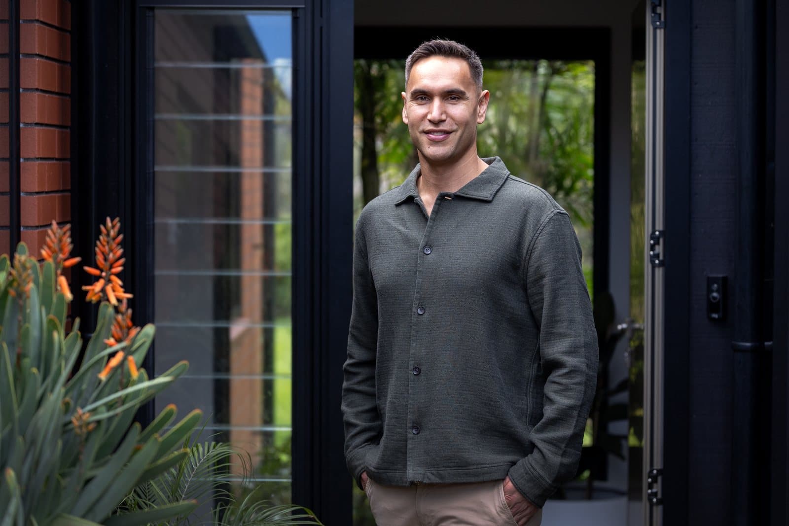 Riki Hoeata standing in a doorway beside garden planting.